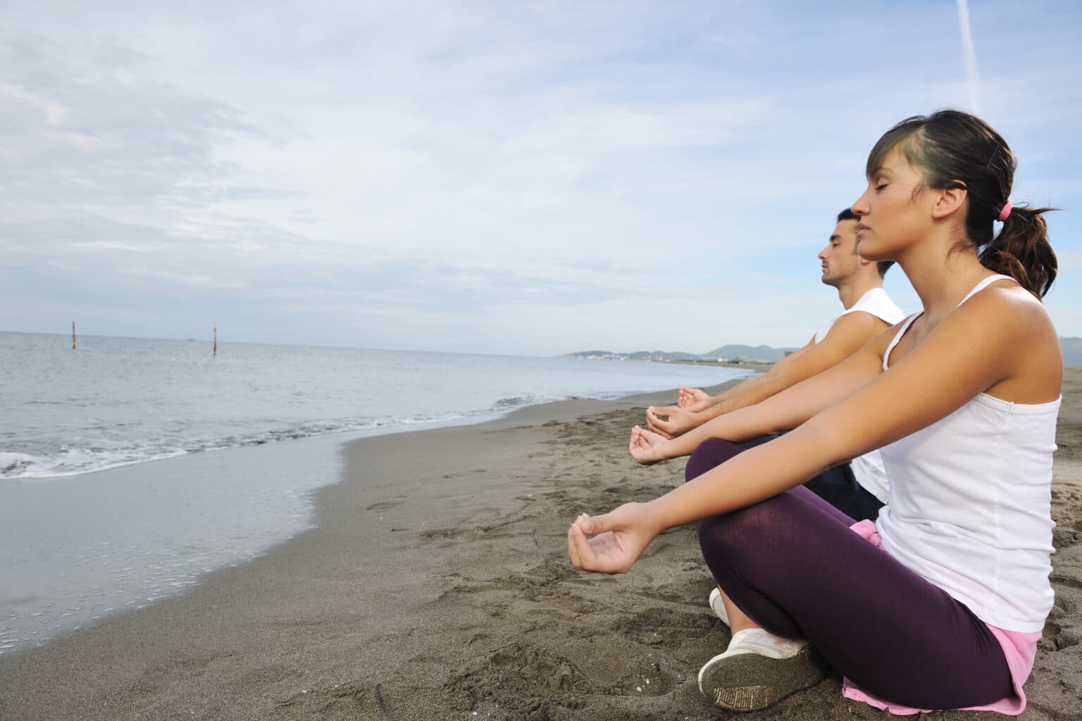Two people practicing yoga together on a beach